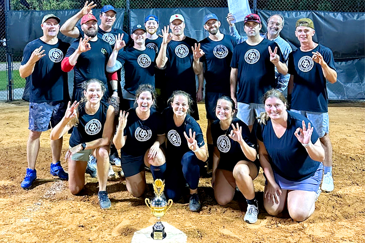Image of Yarborough Applegate softball team, standing and kneeling together on the field with their championship trophy in front of them