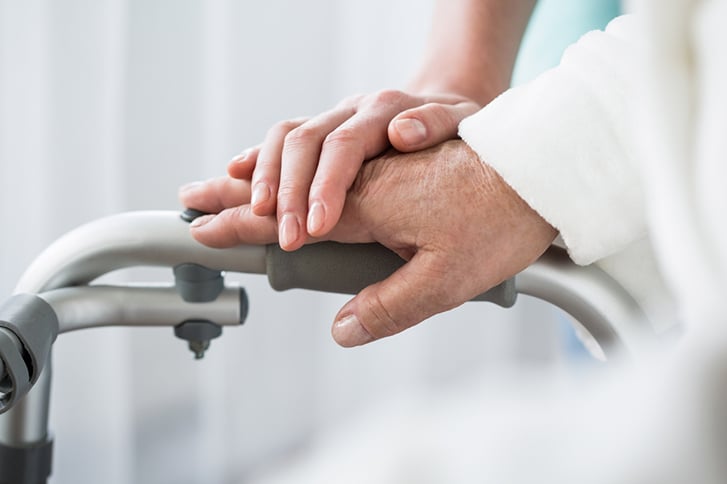 Photo of a person's hand on a walker with another person's hand resting on top